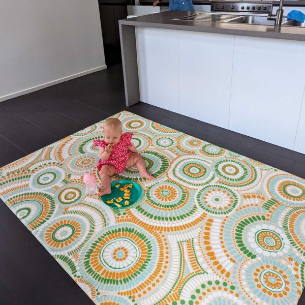 A baby sits on the playmat while eating