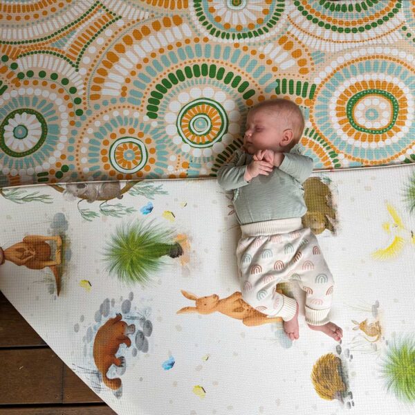 A baby is laying on a rug with a kangaroo on it.